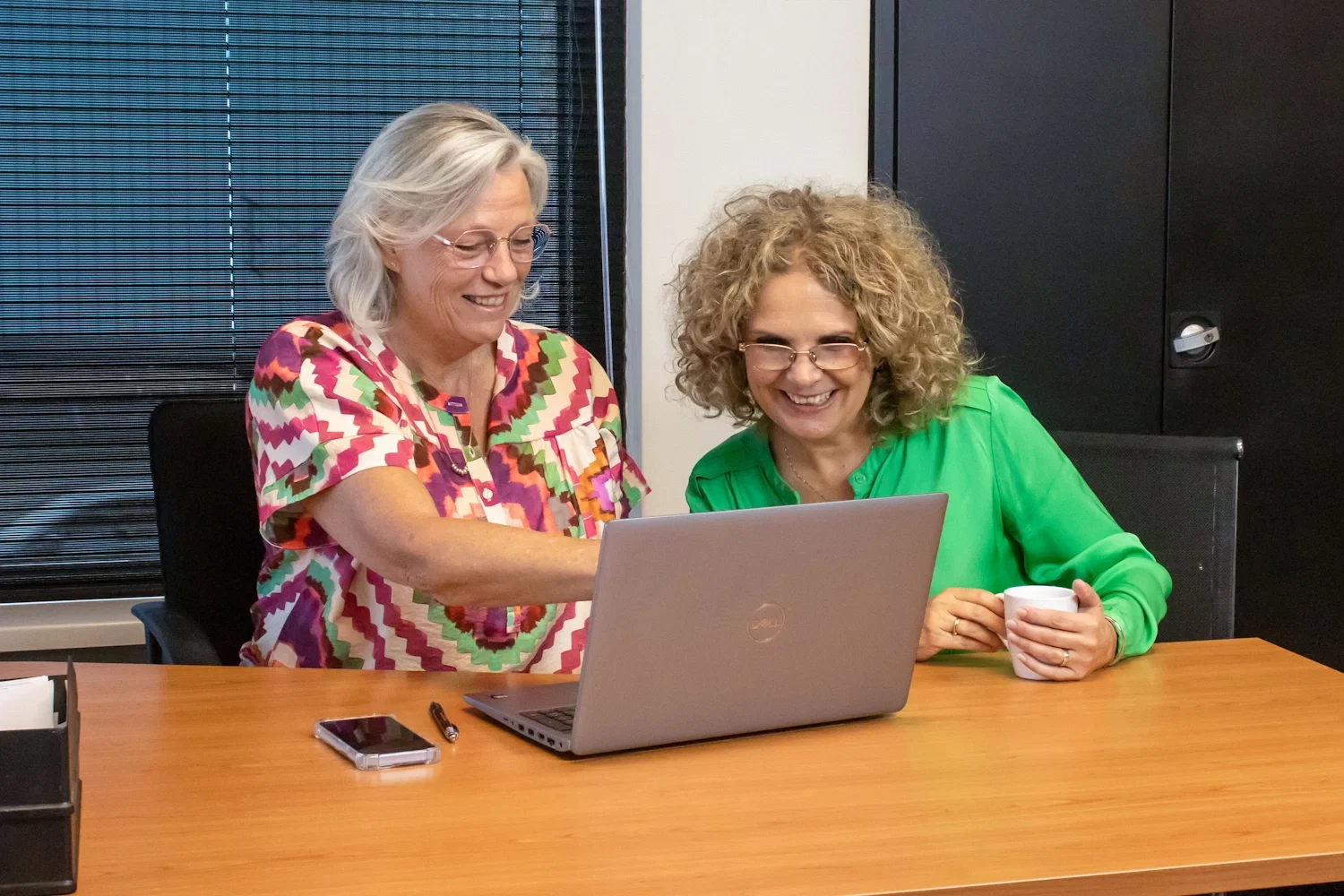 Twee collega's lachend achter een laptop