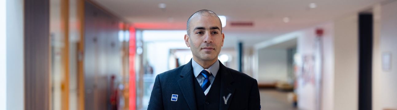 A uniformed security guard is standing in a neat, modern hallway of an office building.