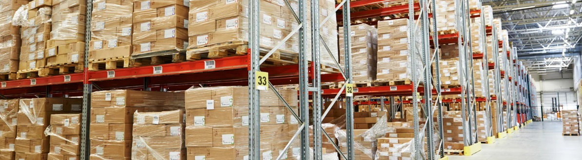 A large storage area with tall warehouse racks filled with pallets and cardboard boxes in a modern distribution center